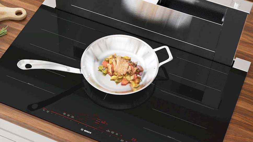 Bosch induction cooktop with chicken cooking on metal pan.