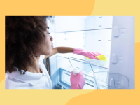 A person wearing rubber gloves wipes down the shelves in a fridge with a cloth