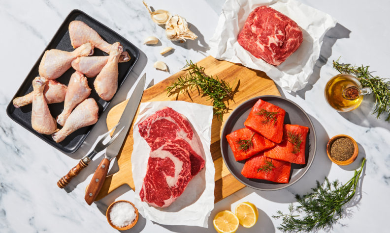 Raw poultry, beef, pork, and salmon on marble countertop.