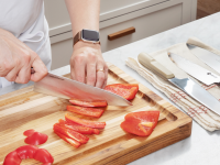 Hand cutting a bell pepper with a chef's knife, beside a line of other chef's knives.