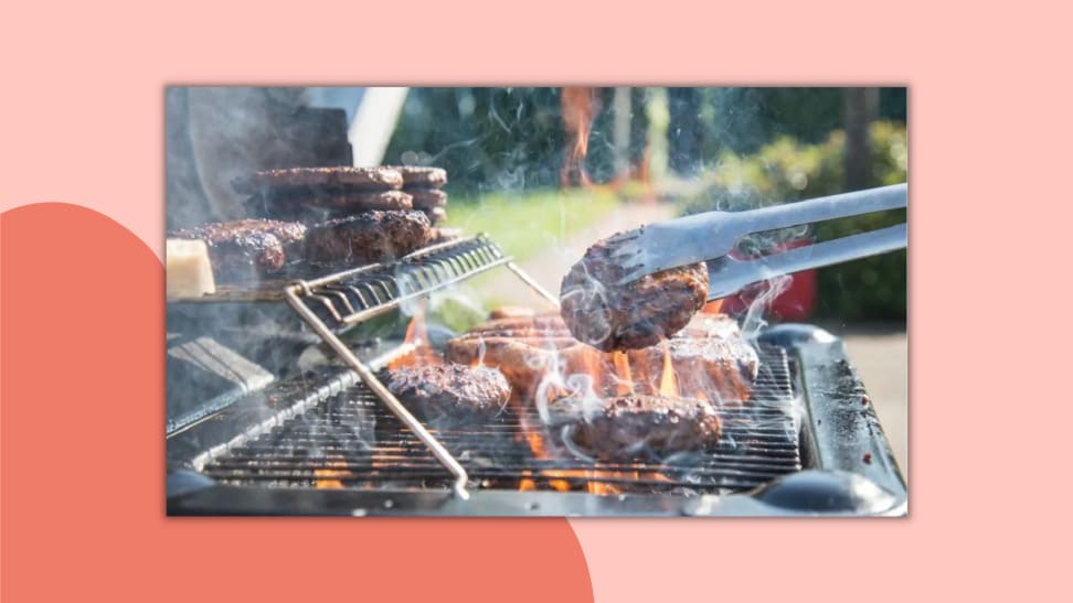 Several burgers cooking on a grill, shot from the side, with a pair of tongs holding a patty.