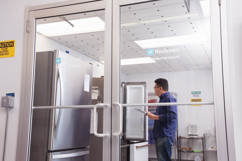 An Asian man with a clipboard stands in a room with glass walls