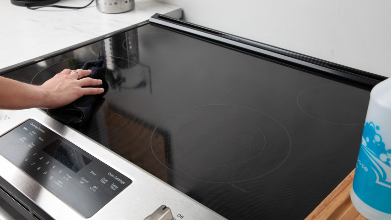 A hand wiping a rag on a clean glass stove.