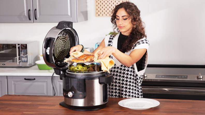 A person places an entree onto a rack inside a multicooker Ninja Foodi.