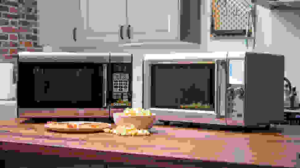 A pair of stainless-steel microwaves sit side by side on a wood-grain countertop.