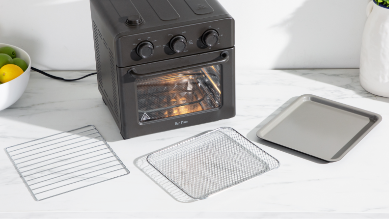 Our Place Wonder Oven sitting on a countertop next surrounded by wire racks and cooking trays.