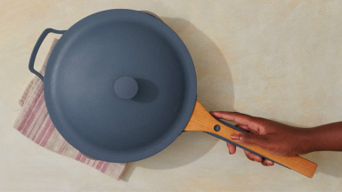 A person grabs the handle of a blue ceramic pan.