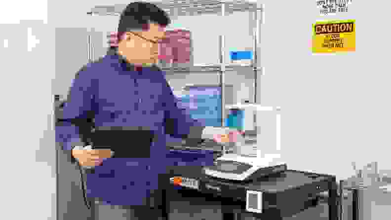 Lab technician placing plastic Tupperware container with floral foam ball inside on scale.