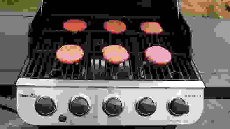 Six raw burger patties laid out on an open gas grill