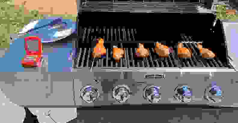 Six chicken drumsticks cooking on a gas grill, one of them hooked up to a probe thermometer